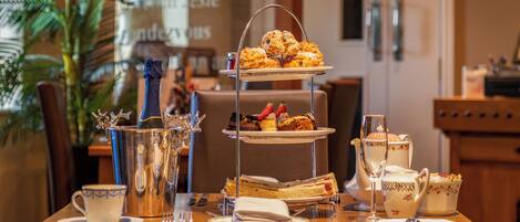 Ein dreistöckiges Kuchenbuffet mit Gebäck, einem Teekännchen, Tassen und einem Glas auf einem Holztisch in einem Essbereich.