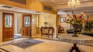 A hotel lobby with a chandelier, a round table with a patterned tablecloth, a floral arrangement, and a reception desk. - Hollins Hall Hotel, Spa & Golf (Shipley)