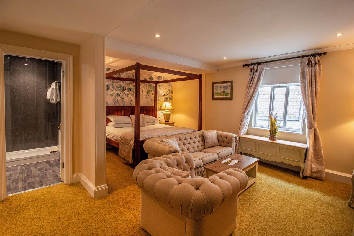 Ein Schlafzimmer mit Himmelbett, Sofa, Nachttisch und einem Fenster mit Vorhängen.