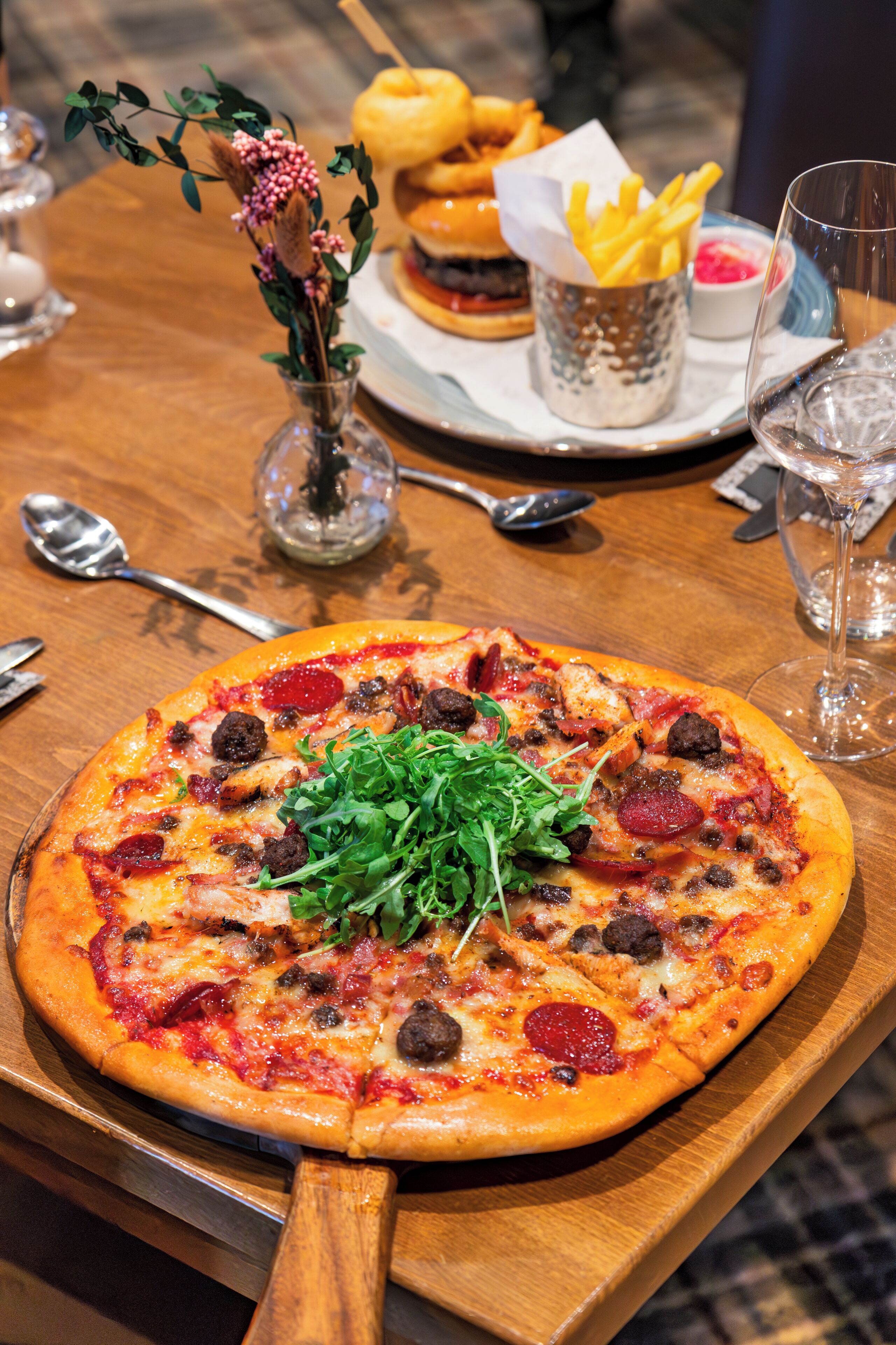 A pizza with toppings, a burger, fries, and a drink on a wooden table.