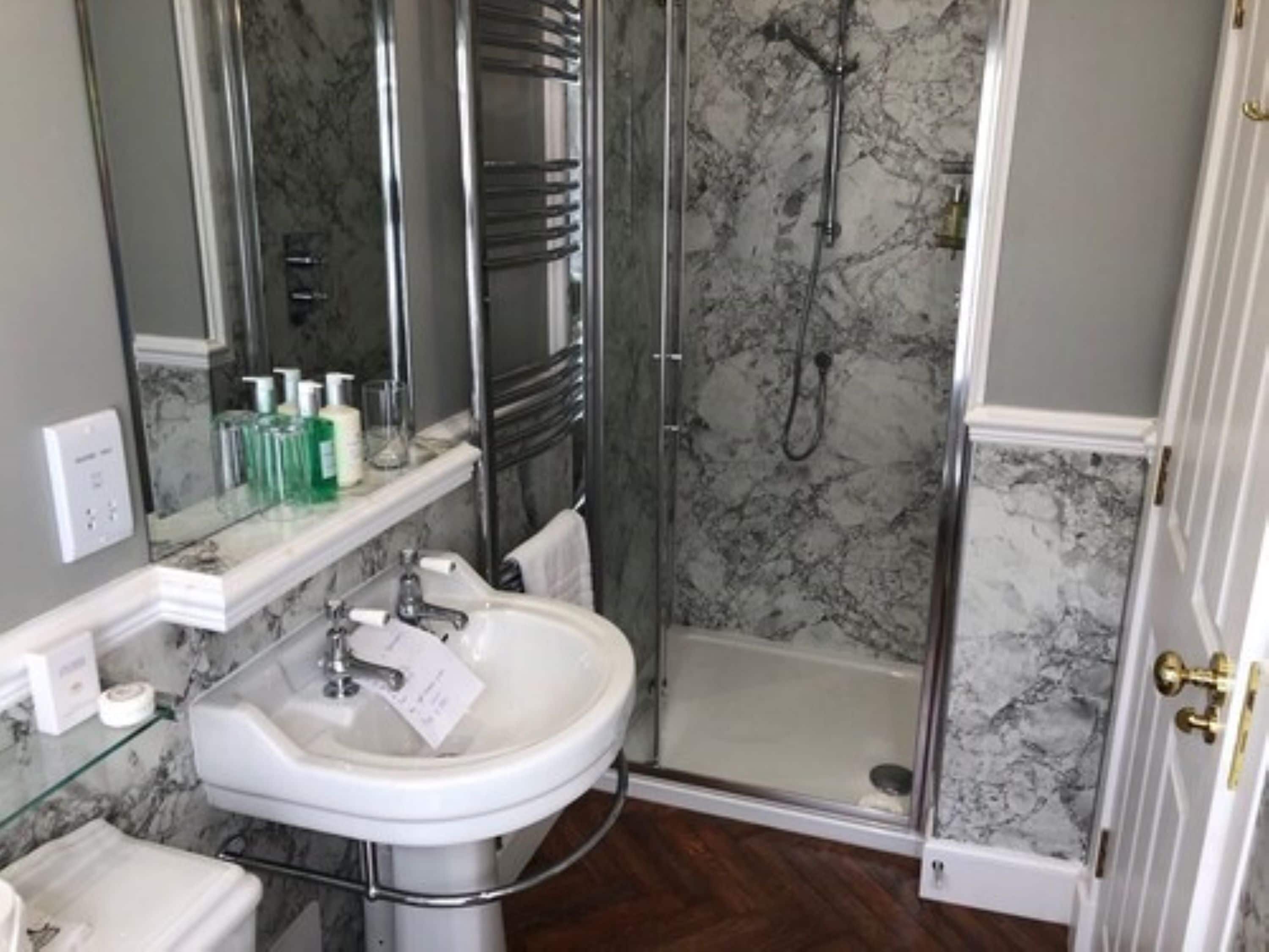 Une salle de bain avec un lavabo blanc, une douche en verre et un pare-baignoire en marbre.
