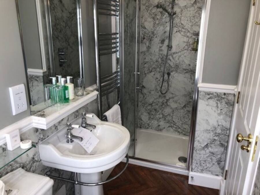 Une salle de bain avec un lavabo blanc, une douche en verre et un pare-baignoire en marbre.