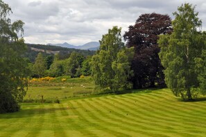 A golf course with a well-maintained lawn, trees, and a distant mountain range.