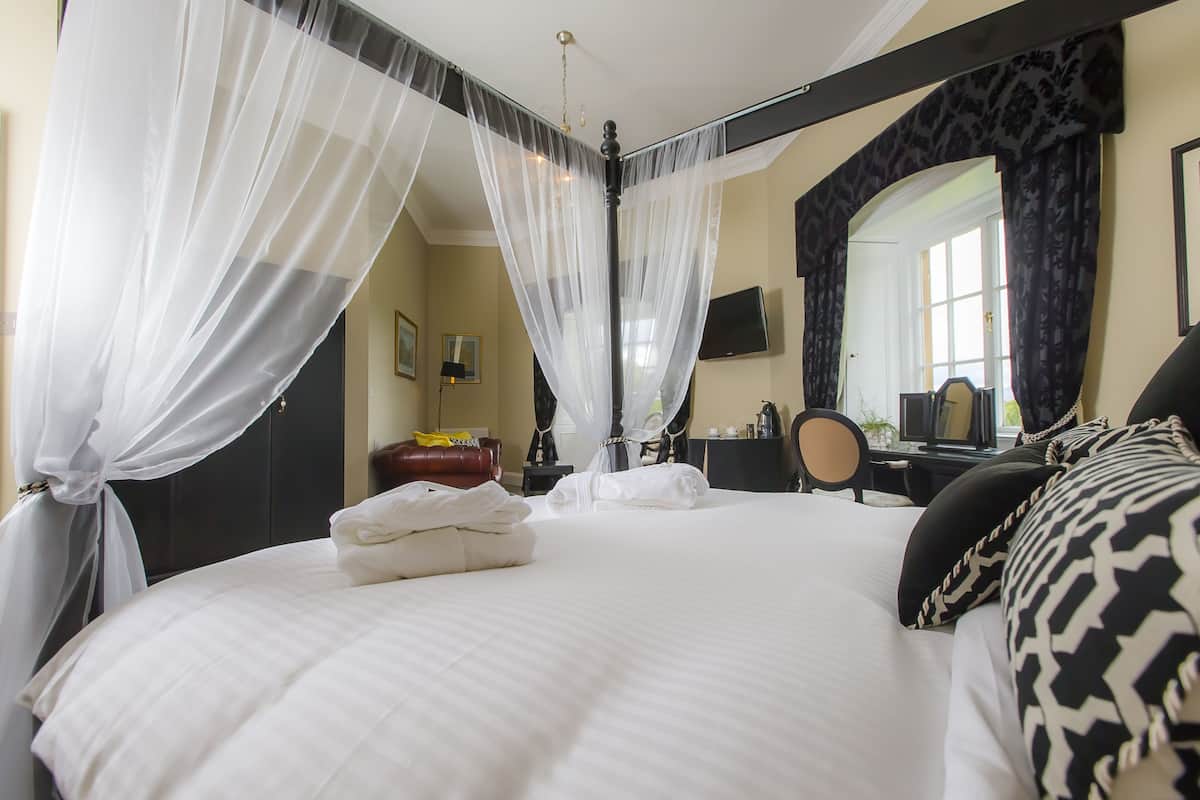 Un lit bien fait, avec du linge de lit blanc, une table de chevet avec une lampe et un miroir au mur.