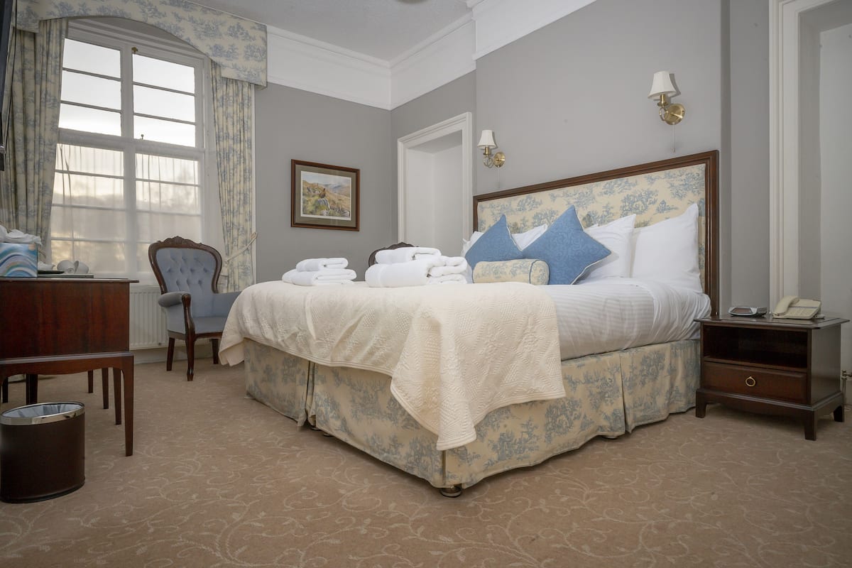 Une chambre d’hôtel bien aménagée, avec un grand lit, une chaise, un bureau et une table de chevet avec une lampe.