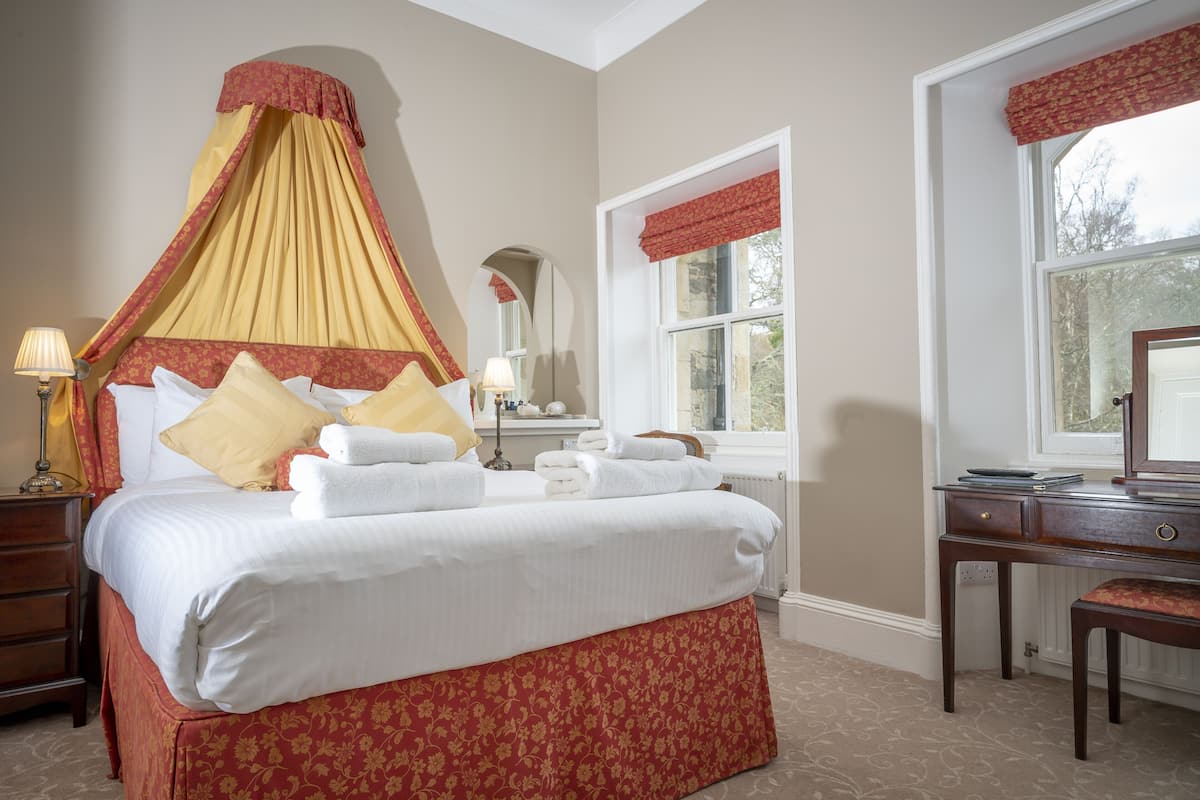 Une chambre à coucher avec un lit à baldaquin, une commode, un miroir et une fenêtre avec des rideaux.