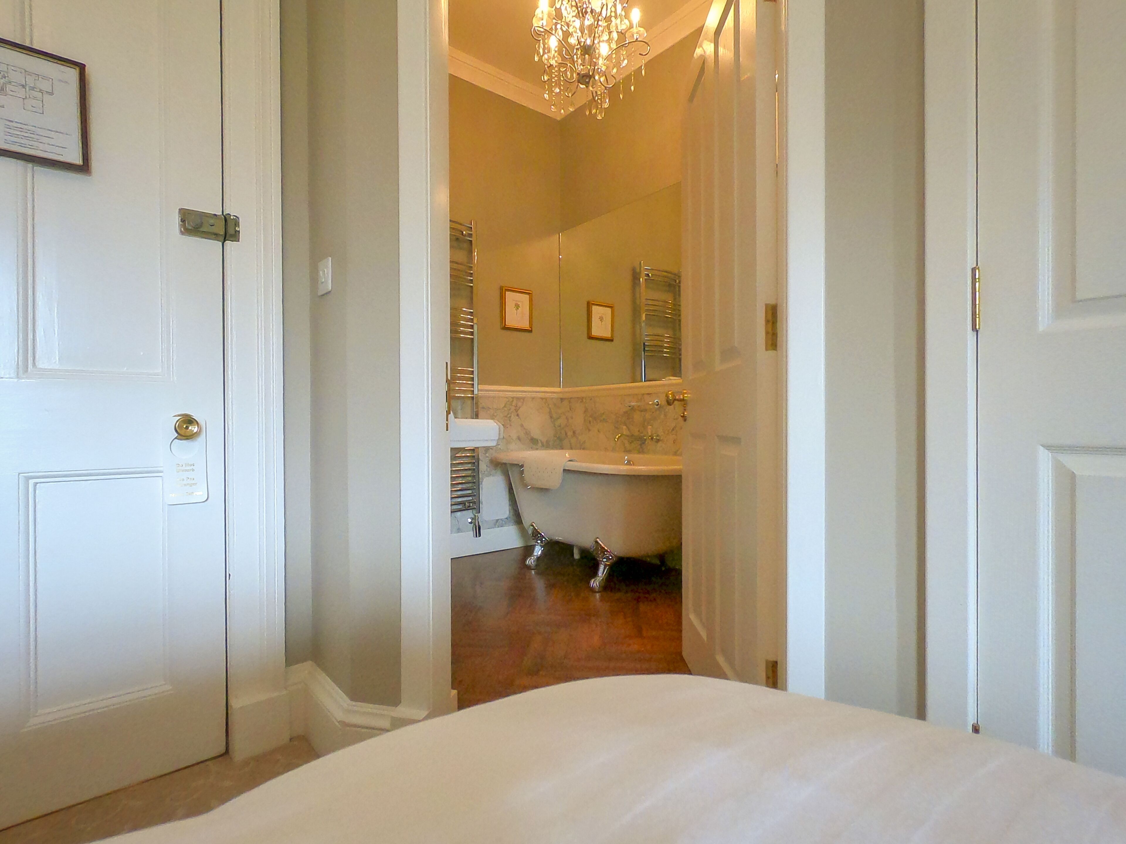 Une chambre d’hôtel avec un grand lit, une salle de bain avec baignoire, un lustre et un certificat encadré accroché à la porte.