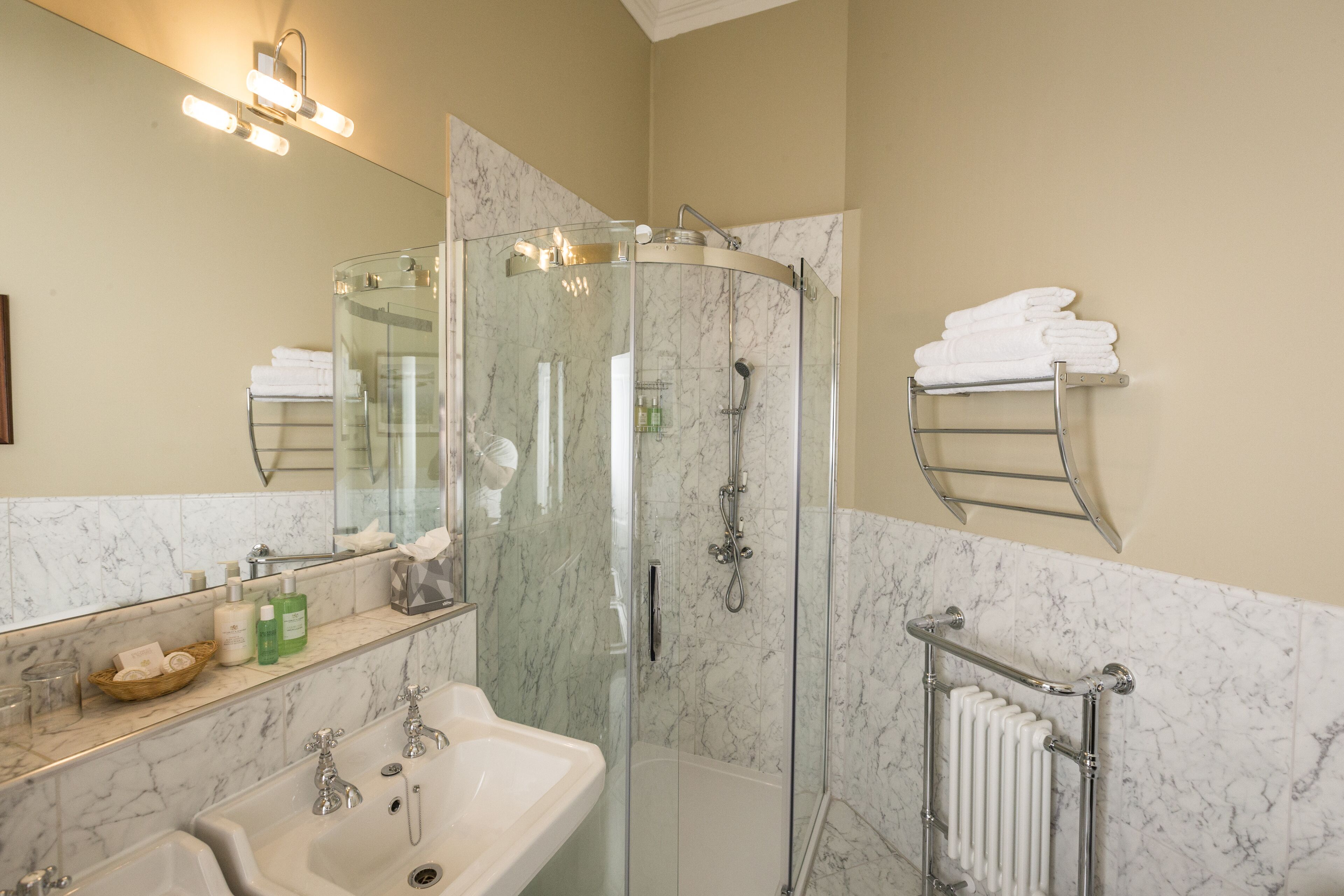 A bathroom with a glass-enclosed shower, a sink, a mirror, and a towel rack.