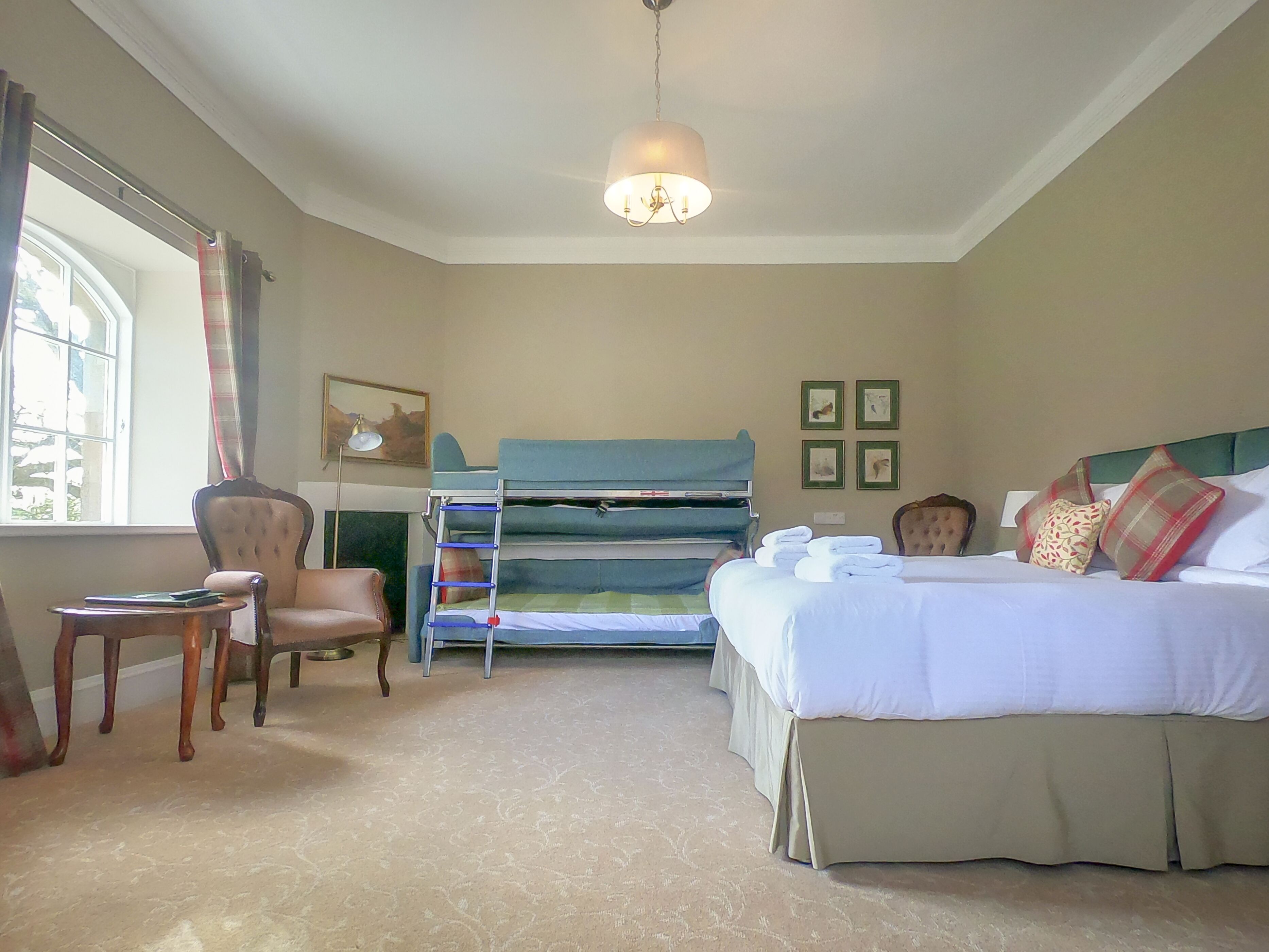 A hotel room with a bunk bed, a desk, a chair, a lamp, and a bed with pillows and a blanket.