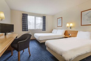 A hotel room with two beds, a desk, a chair, a television, and a window with curtains.