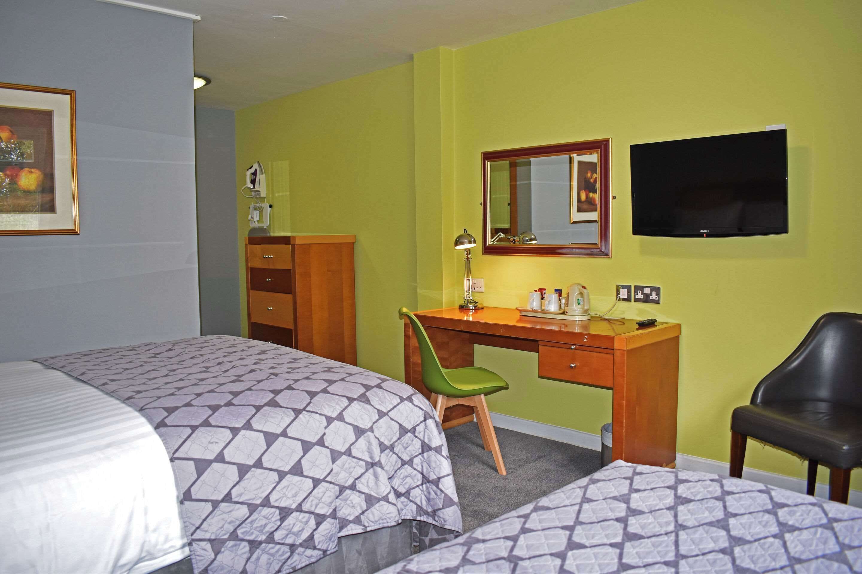 A hotel room with two beds, a desk with a chair, a television, and a mirror.