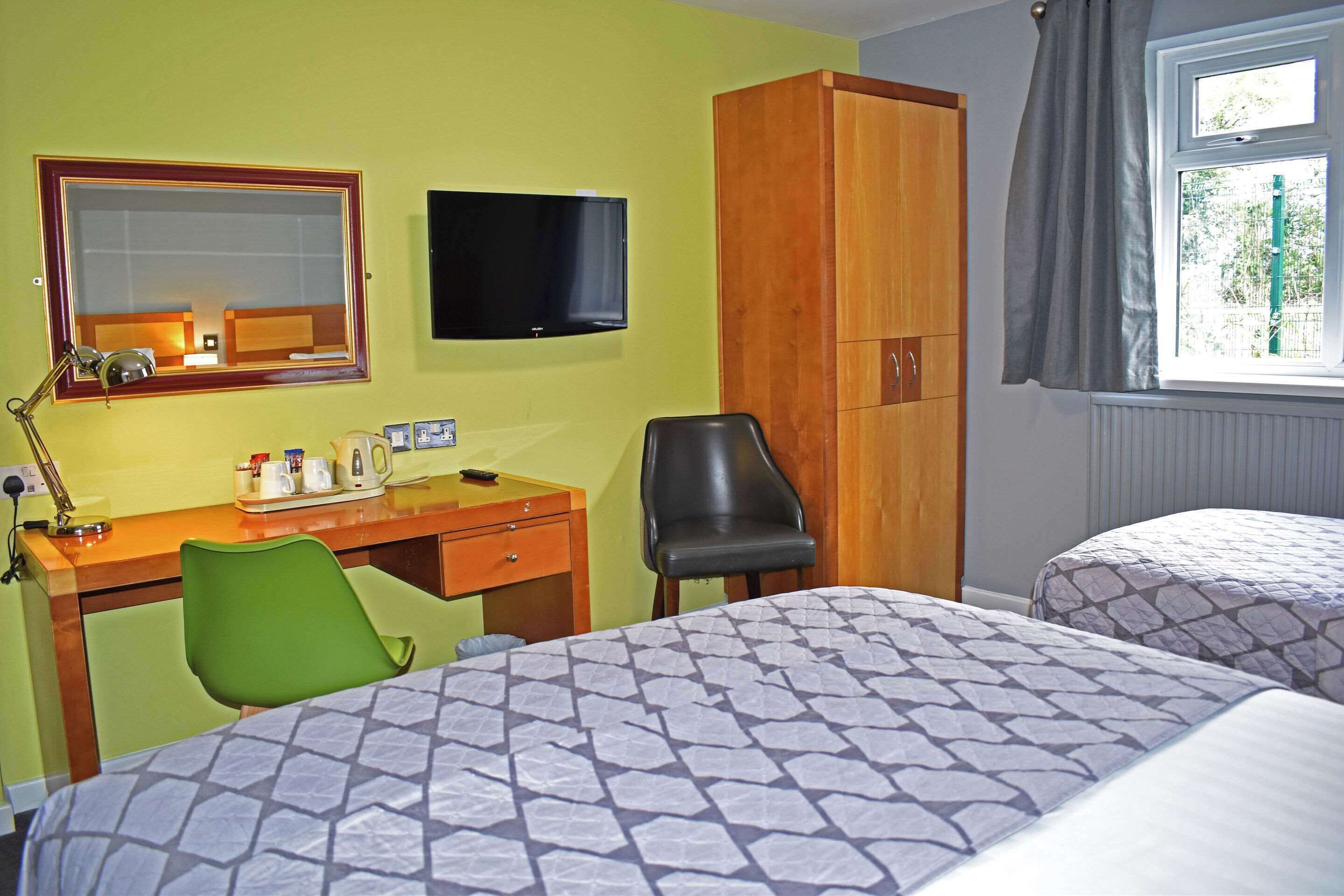 A hotel room with two beds, a desk with a chair, a television, and a window with curtains.