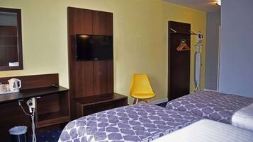 A hotel room with two beds, a TV mounted on the wall, a desk with a kettle, and a chair.