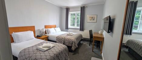 A hotel room with two beds, a desk, a chair, a TV, and a window with curtains.