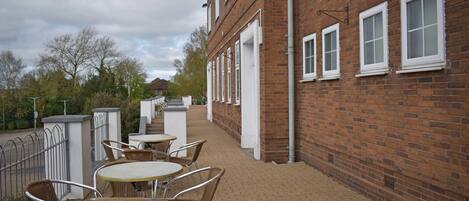 A brick building with a paved patio, outdoor seating, and a metal fence.