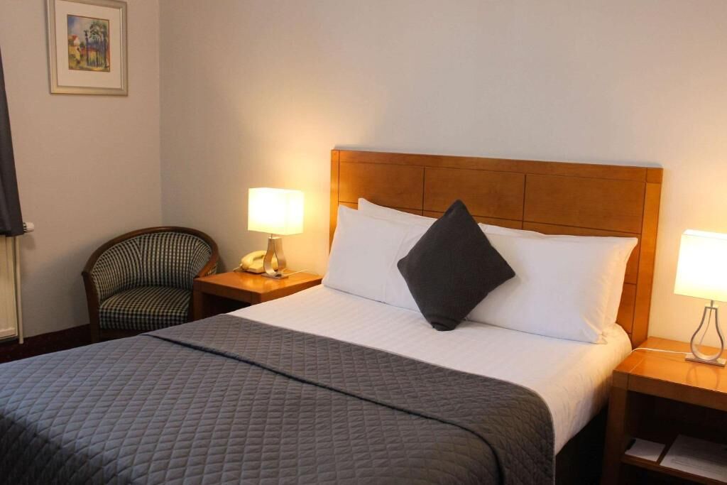 A hotel room with a large bed, two bedside lamps, a chair, and a framed picture on the wall.