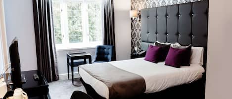 A hotel room with a large bed, a desk with a computer, a chair, and a window with curtains.