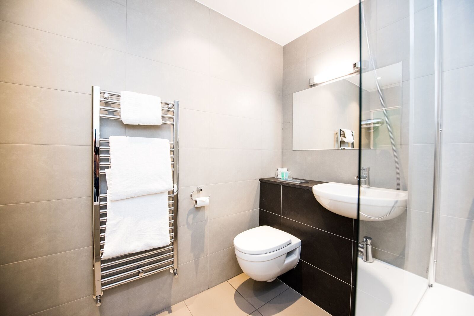Un baño moderno con cabina de ducha de vidrio, inodoro blanco y lavamanos negro.