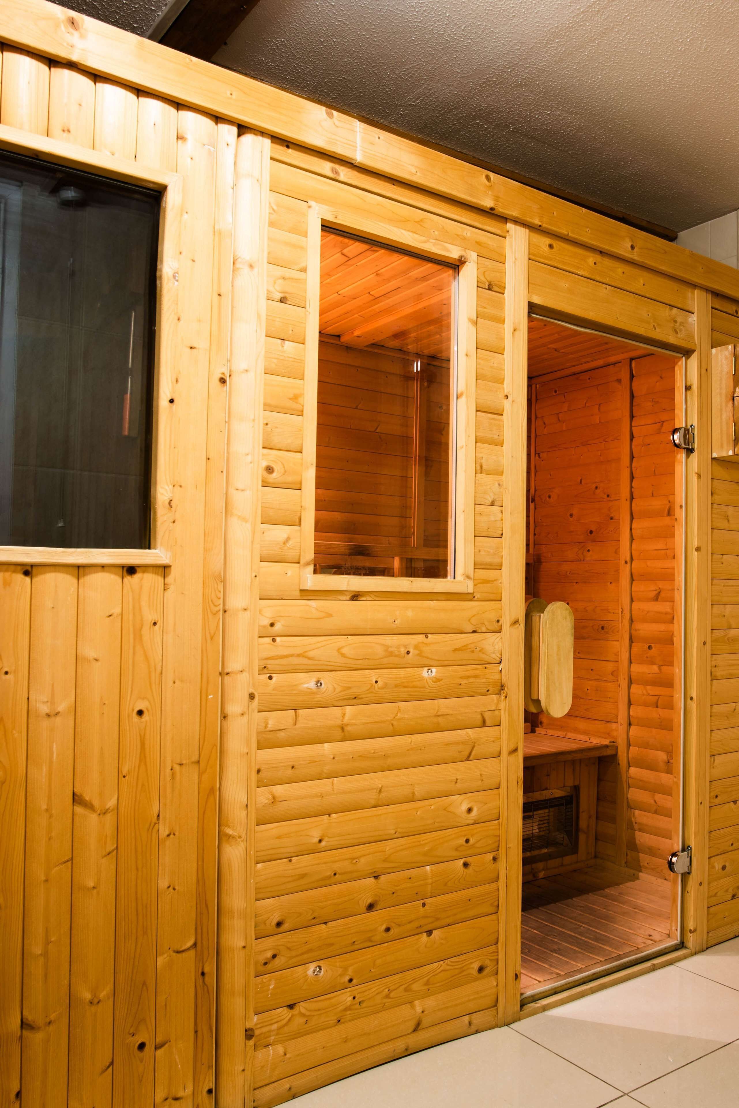 A wooden sauna with a glass door, a bench inside, and a tiled floor.