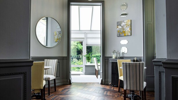 A hallway with a herringbone wood floor, a chandelier, and a dining area with chairs and a table.