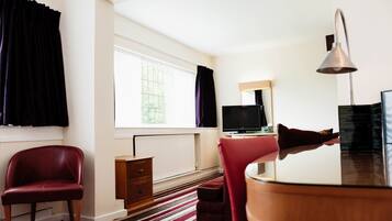 A hotel room with a large window, a flat-screen TV, a wooden desk, a red chair, a small cabinet, and a striped rug.