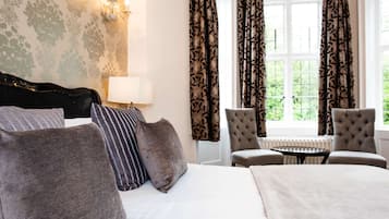 A hotel room with a bed, two armchairs, a small table, a lamp, and curtains.