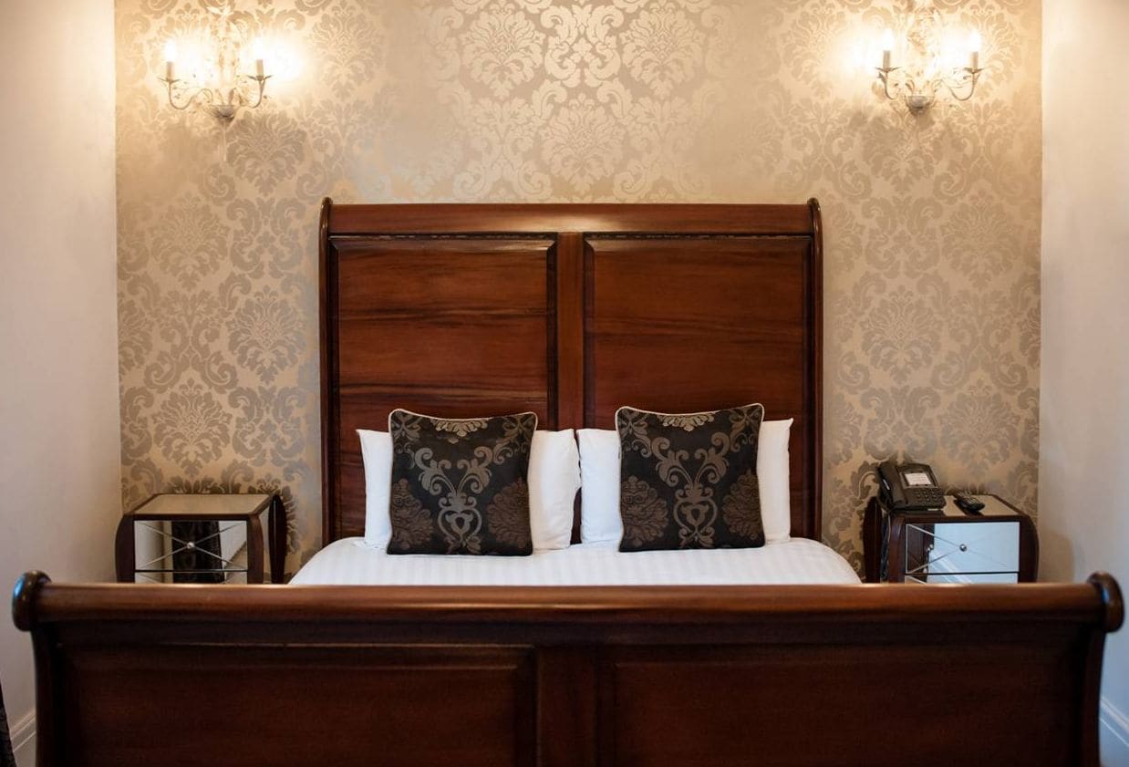 A double bed with a wooden headboard, two bedside tables, and a patterned wallpaper.