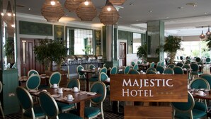 A spacious hotel dining area with multiple tables and chairs, large hanging lights, and a sign reading "MAJESTIC HOTEL".