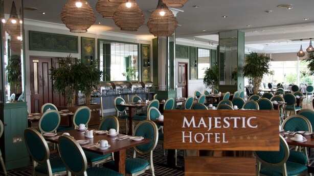 Un amplio comedor de hotel con varias mesas y sillas, grandes lámparas colgantes y un letrero que dice "MAJESTIC HOTEL".