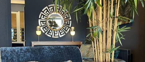 Un salón moderno con un sofá azul oscuro, un espejo decorativo y una planta de bambú grande.