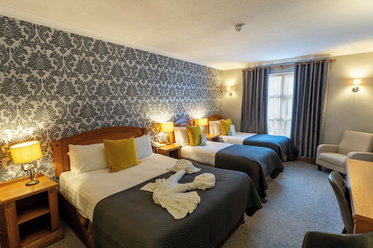 A hotel room with two beds, a desk, a chair, and a lamp.