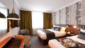 A hotel room with a large bed, a smaller bed, a desk with a chair, a dining table with breakfast items, and a large mirror.