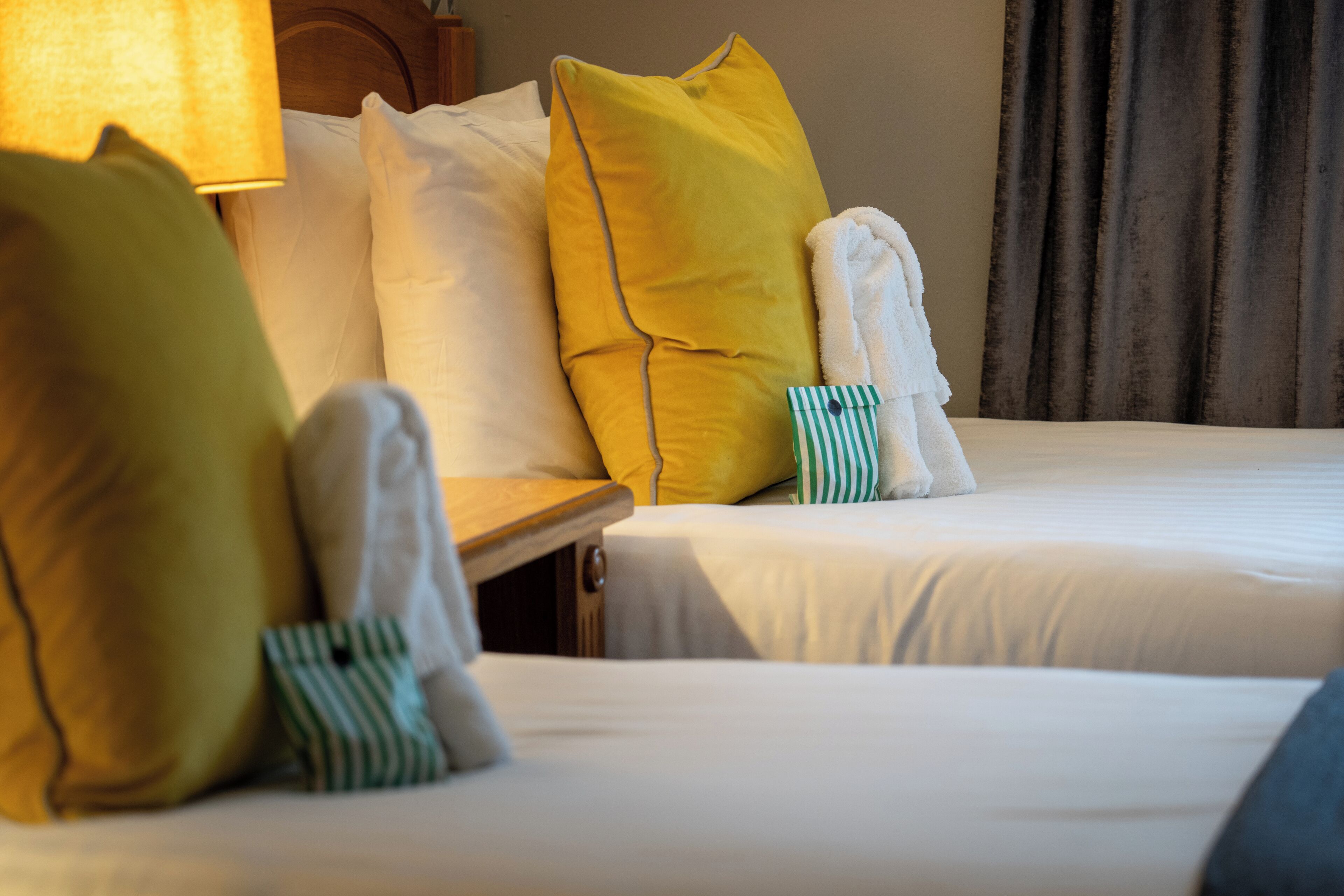A hotel room with two beds, each with white linens and multiple pillows in various colors.