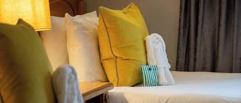 Habitación de hotel con dos camas, cada una con ropa blanca y varias almohadas de distintos colores.