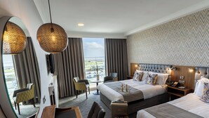 A hotel room with two beds, a desk, a chair, a mirror, and a view of the outside.