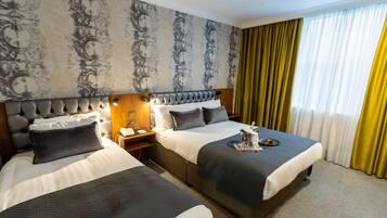 A hotel room with two beds, a headboard with a light fixture, a nightstand with a phone and a glass of water, and a window with yellow curtains.