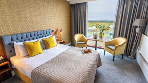 A hotel room with a large bed, two chairs, a table with a vase of flowers, and a view of the landscape.