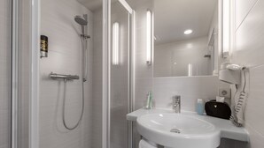 Un baño moderno con ducha acristalada, lavamanos blanco y espejo.