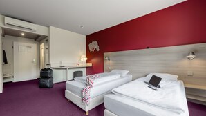 Habitación de hotel con dos camas, un escritorio y una silla. Presenta una pared de acento roja y un techo blanco.