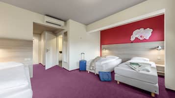 Ein Hotelzimmer mit zwei Betten, einem violetten Teppich, einer roten Akzentwand und einem blauen Koffer.
