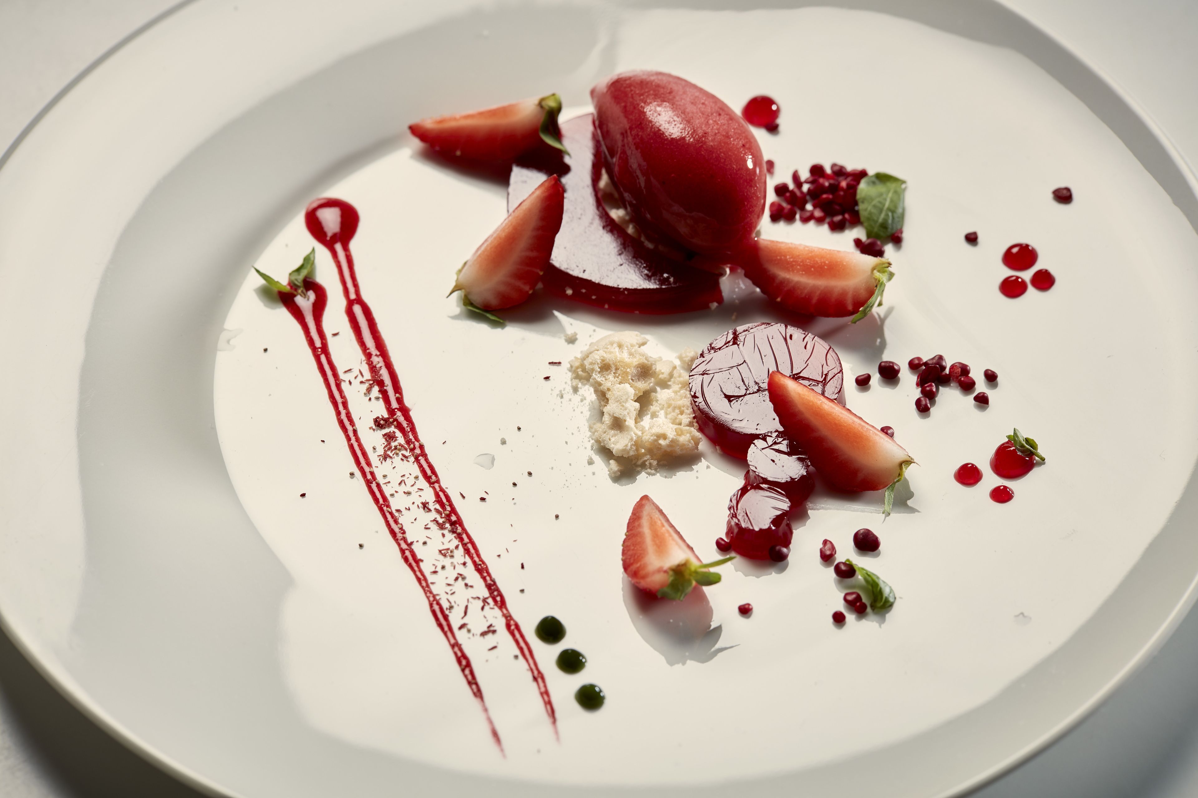 A dessert plate with strawberries, a scoop of ice cream, and a red sauce.