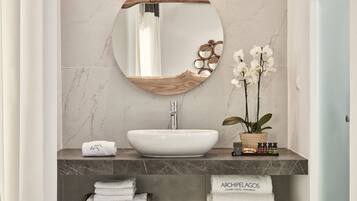 Een badkamer met een ronde spiegel, een witte wastafel en een orchidee in pot.