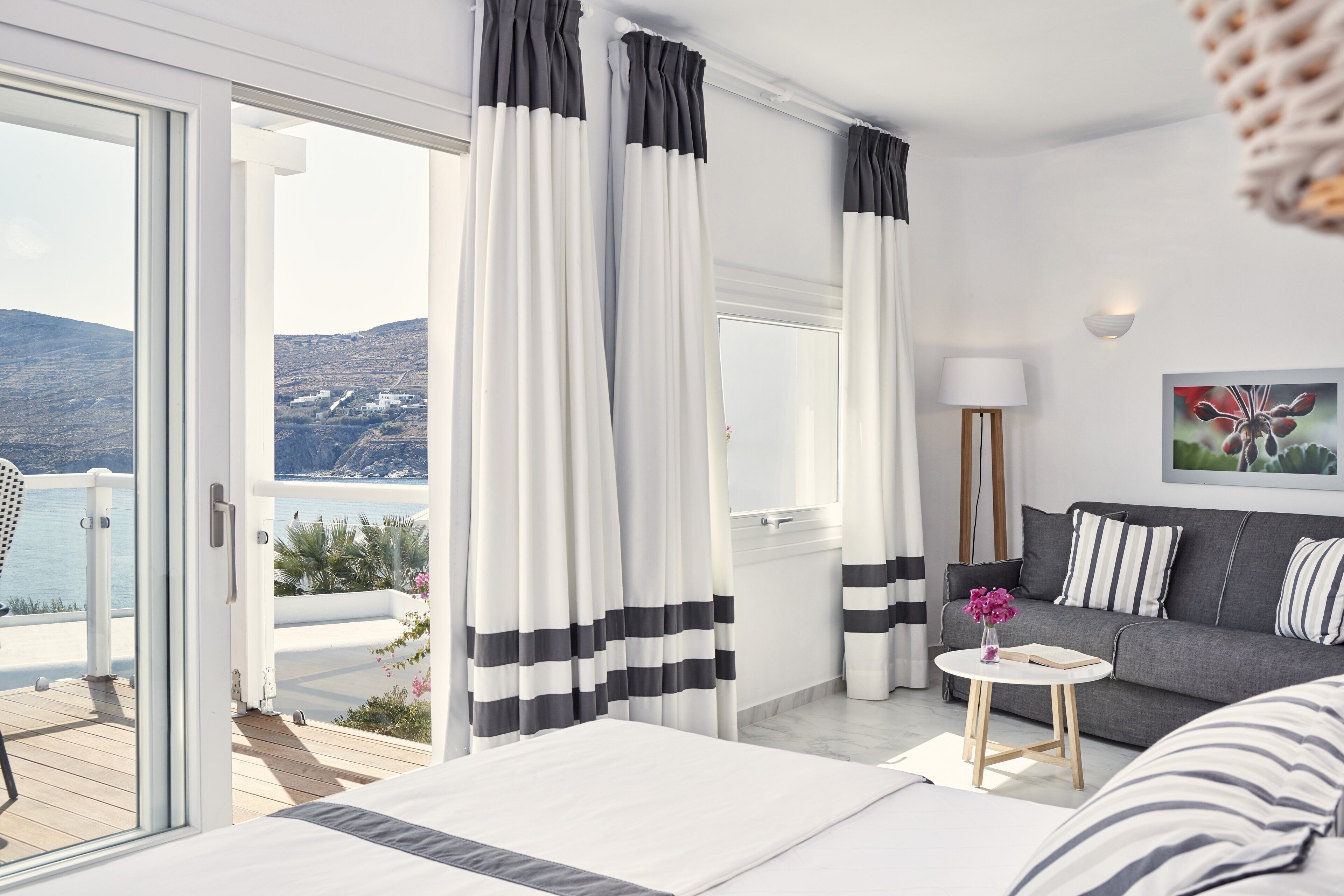 A modern hotel room with a balcony, a sofa, a small round table, and a bed.