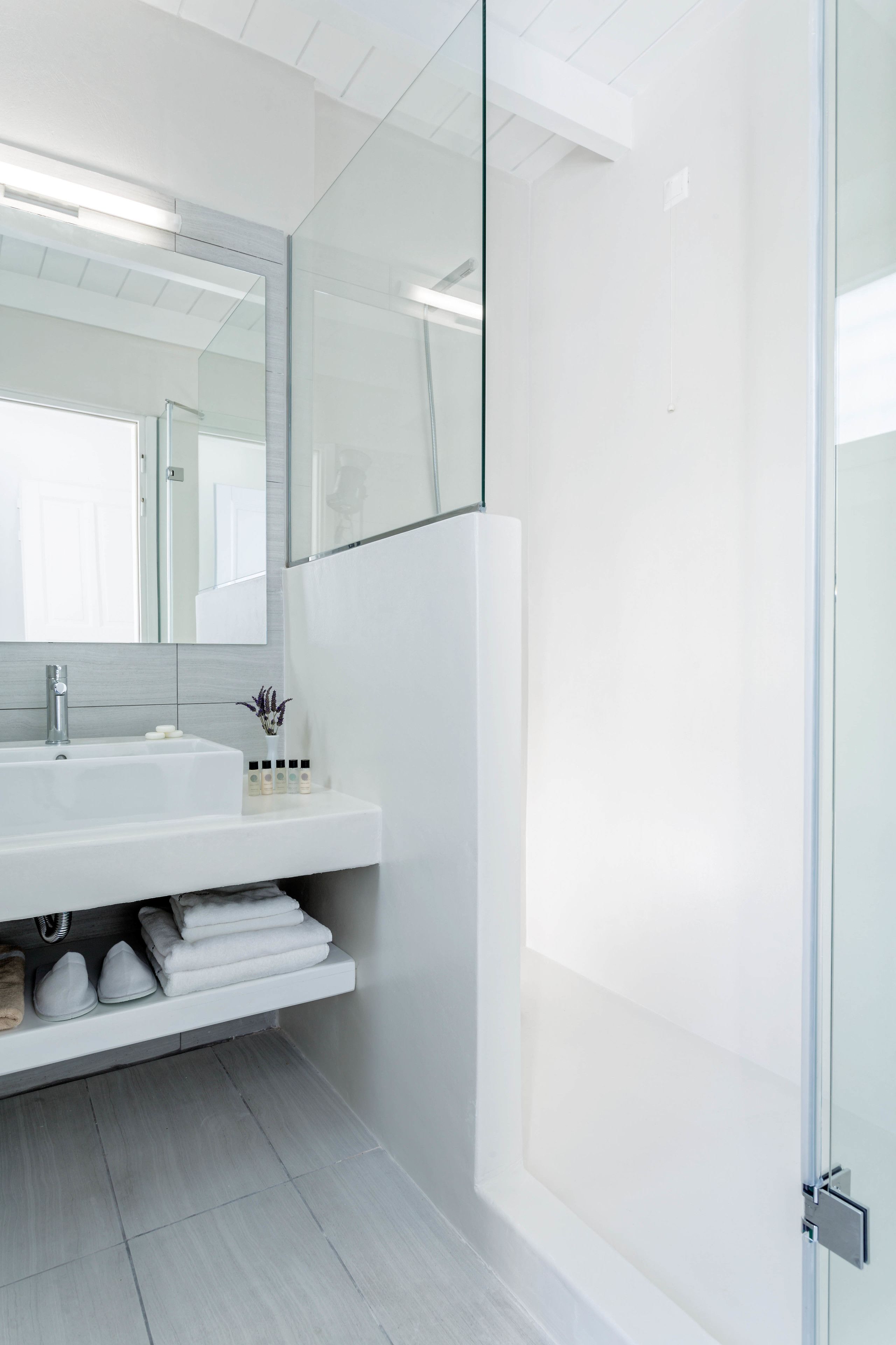 Un baño moderno con lavamanos blanco, espejo y cabina de ducha con mampara de vidrio.