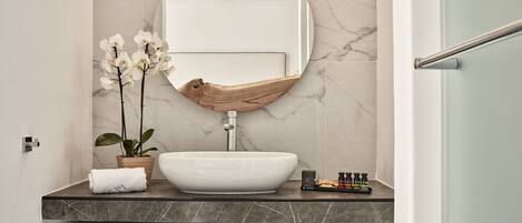 A bathroom with a white vessel sink, a wooden-framed mirror, a potted orchid, and two towels with "ARCHIPELAGOS LUXURY HOTEL MYKONOS" text.