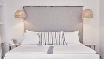 Una cama bien hecha con ropa blanca y almohadas a rayas, dos mesitas de noche con lámparas, y una pared lisa.