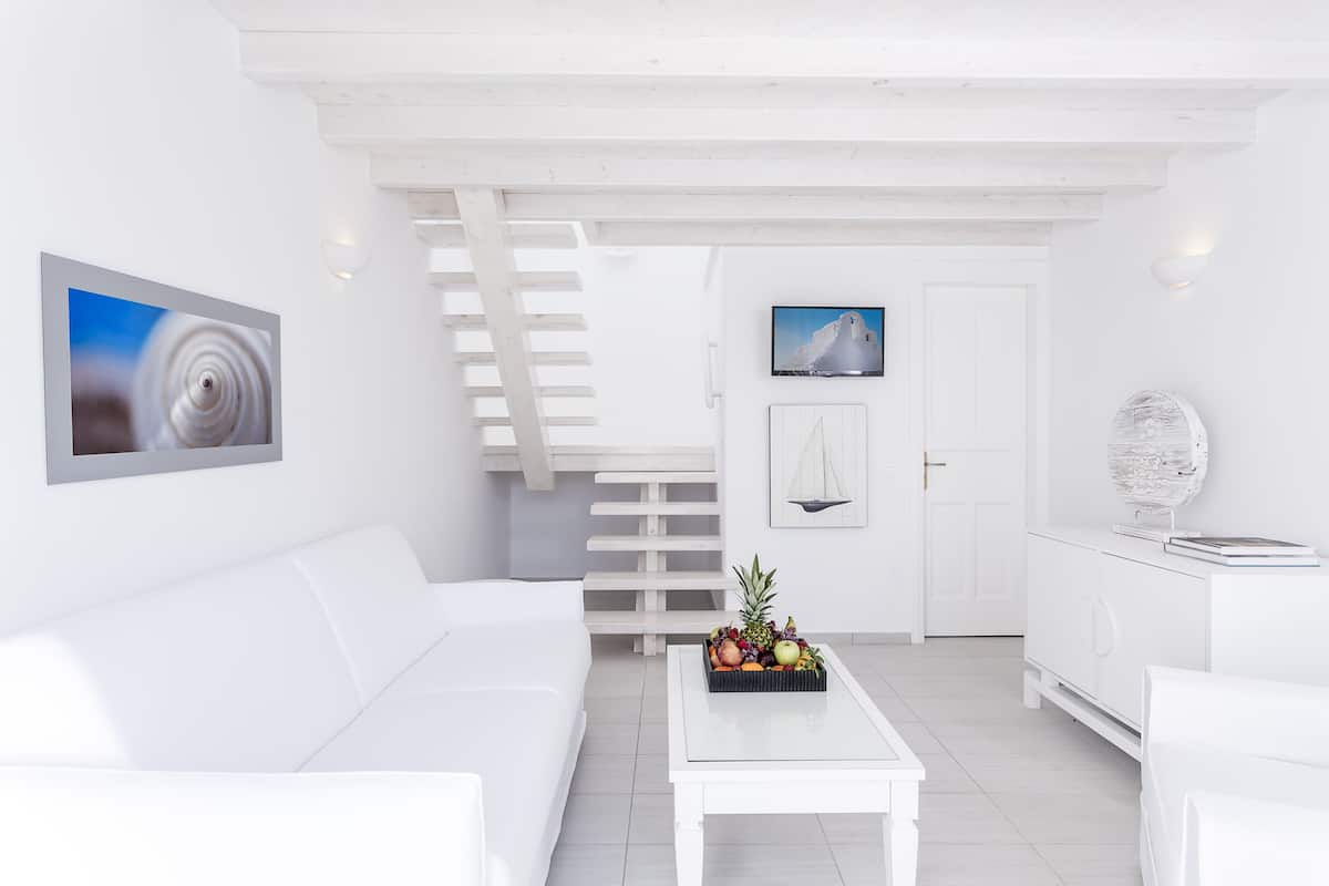 Una sala de estar moderna, decorada en tonos blancos, con un sofá, una mesa de centro y una escalera que conduce a otra habitación.