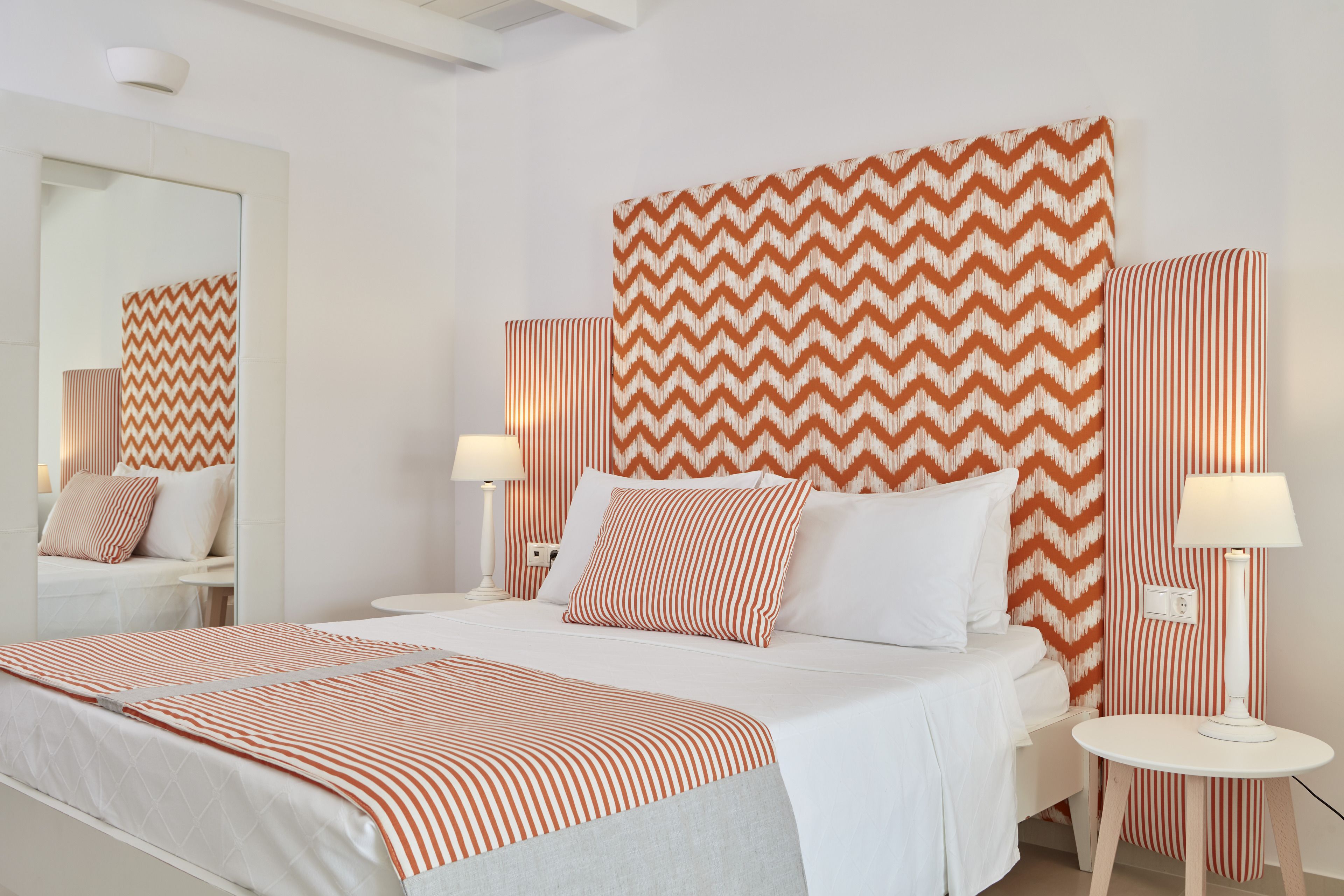 Una habitación de hotel con una cama grande, dos mesitas de noche, un espejo y un cabecero estampado.