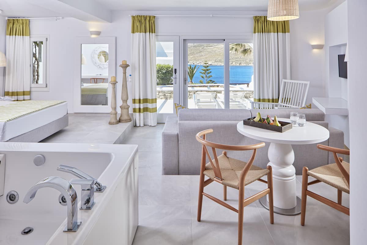 Un hotel moderno con una bañera grande, un comedor con una mesa redonda y sillas, y vistas al mar a través de las ventanas.