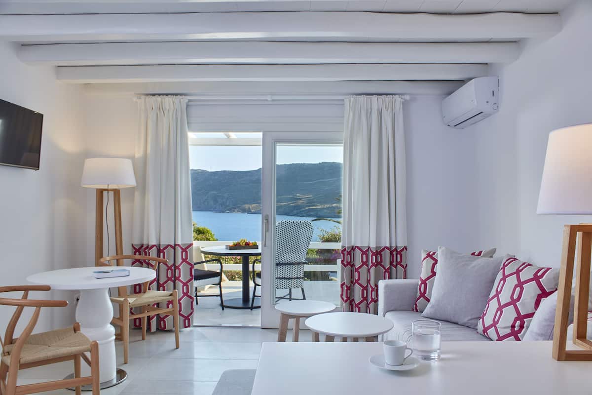Una habitación moderna con balcón, muebles blancos y vista al mar.